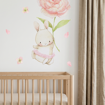 Watercolor bunny holding a pink peony fabric wall decal installed above a wooden crib in a nursery