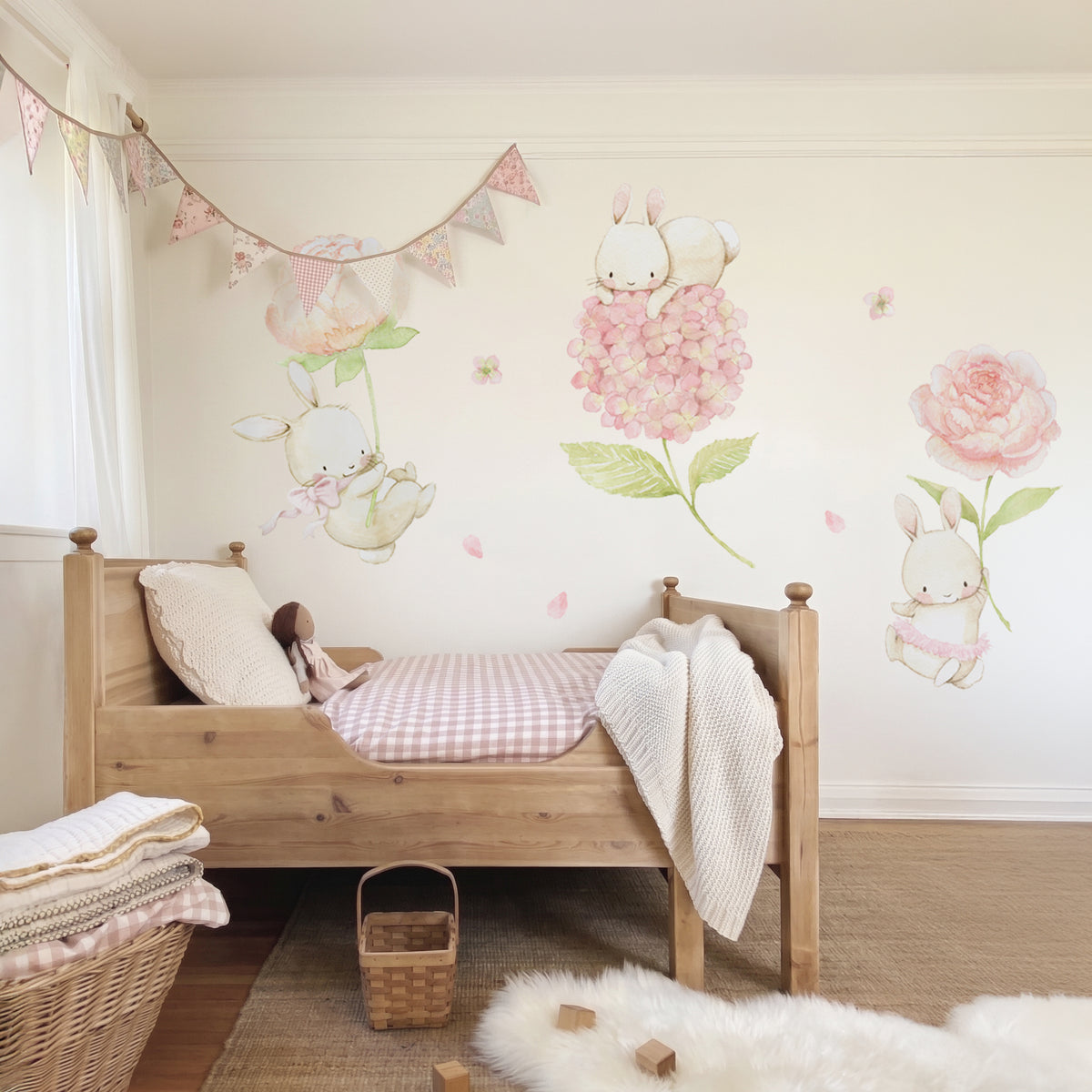 Floral bunnies fabric wall decal set featuring watercolor bunnies holding large pink flowers, arranged on a beige wall above a wooden toddler bed