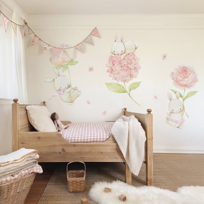 Floral bunnies fabric wall decal set featuring watercolor bunnies holding large pink flowers, arranged on a beige wall above a wooden toddler bed