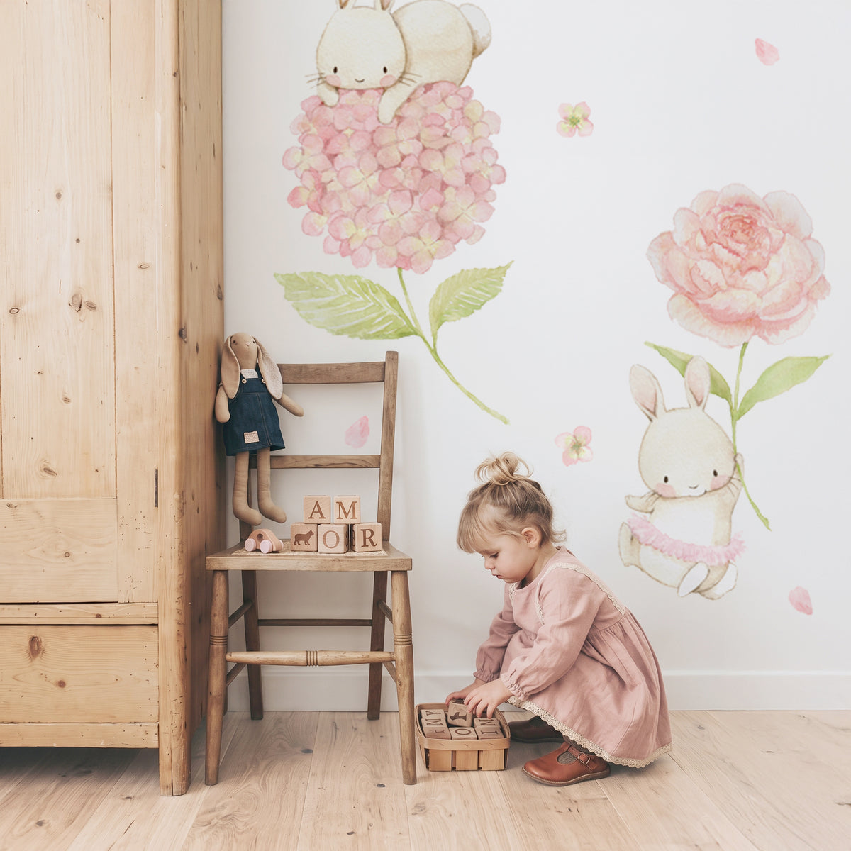 Little girl playing with wooden blocks on the floor under floral bunny watercolor fabric wall decals in a toddler nursery