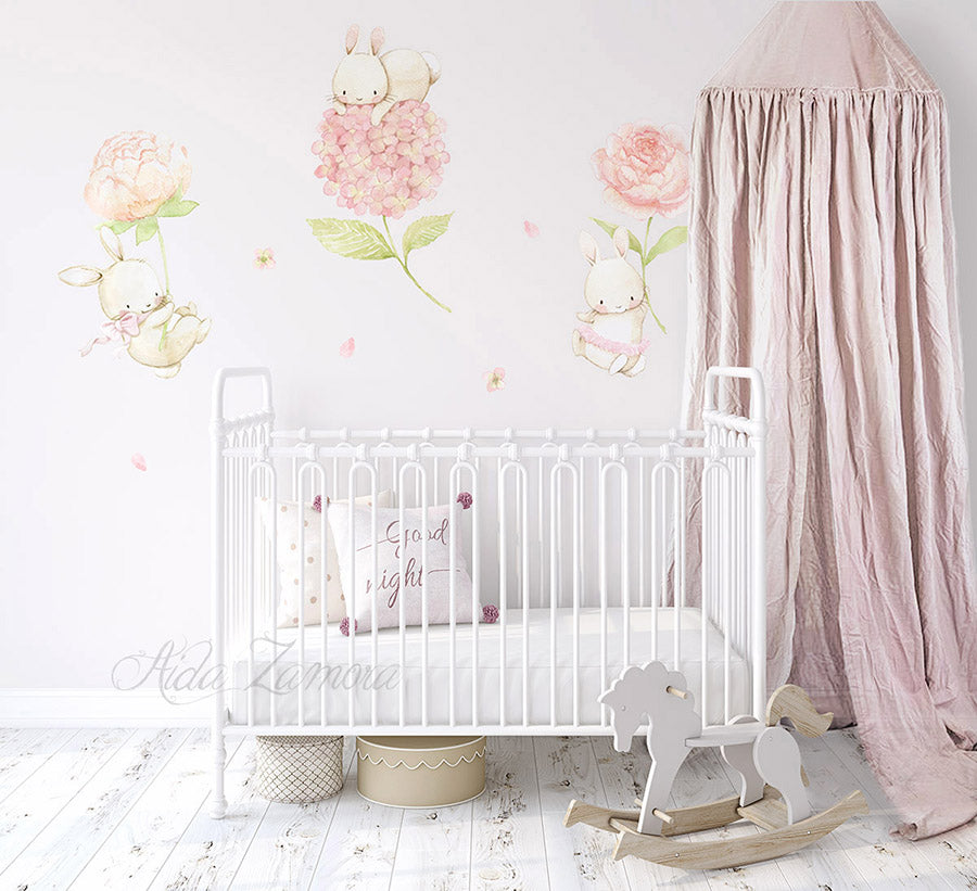 Watercolor floral bunnies fabric wall decals installed on a wall above a white metal baby crib with pink canopy