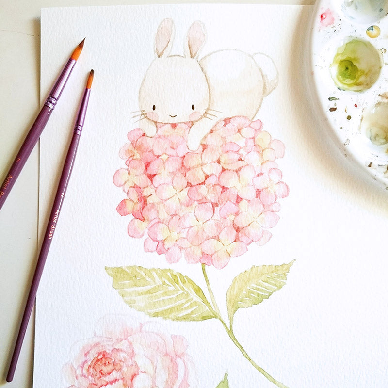 Hand-painted original watercolor illustration of a bunny on a pink hydrangea flower with paintbrushes and palette