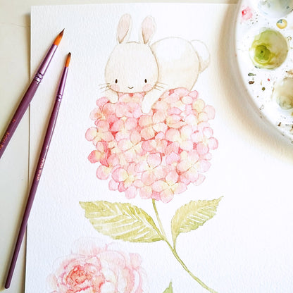 Hand-painted original watercolor illustration of a bunny on a pink hydrangea flower with paintbrushes and palette