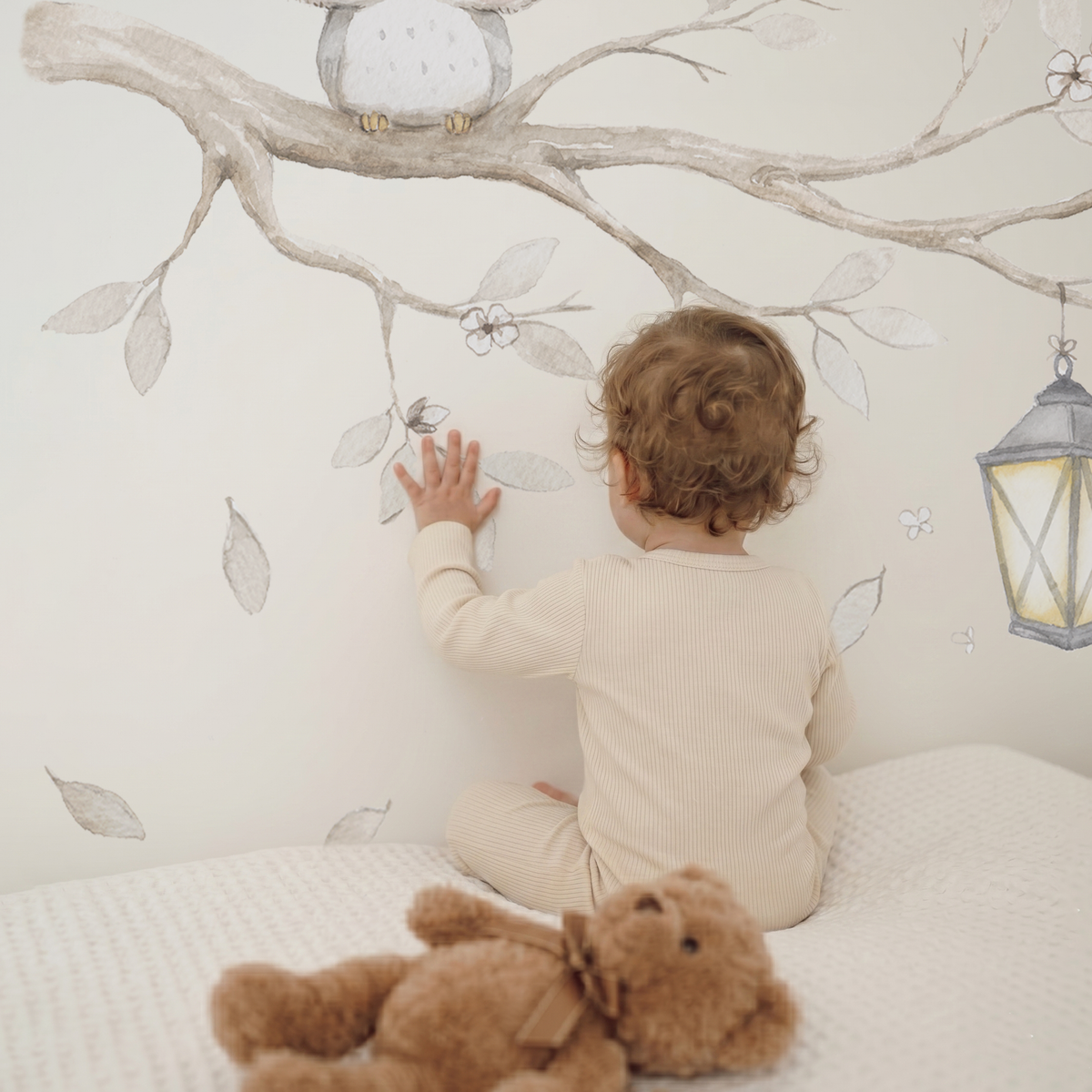Baby touching a watercolor tree branch fabric wall decal set with owl and lantern in a cozy neutral nursery