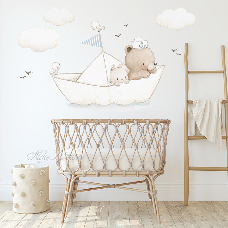 Paper Boat fabric wall decal set featuring watercolor teddy bear sailor, bunny, and clouds arranged on a white wall above a natural wicker baby crib and a wooden ladder