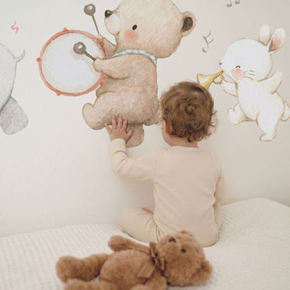 Toddler seen from behind touching the bear decal from the Animal Music Band set on a nursery wall, with a plush bunny toy sitting on the floor
